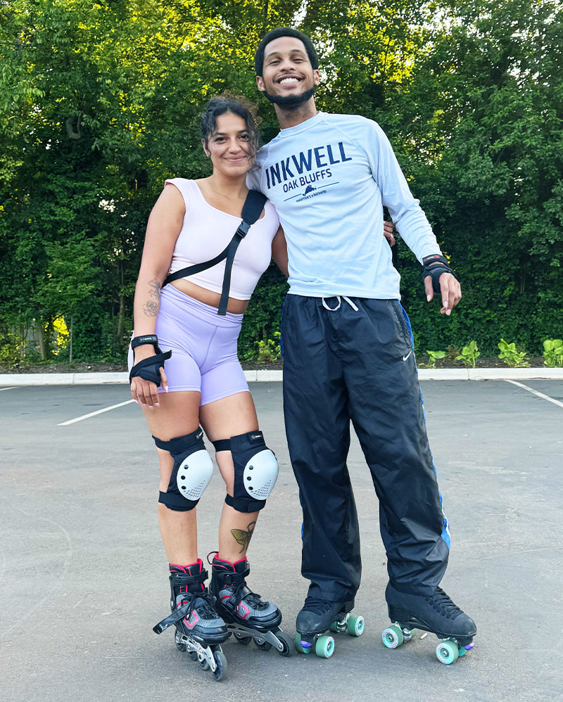 Smiling man and woman wearing roller skates and protective gear posing outdoors.