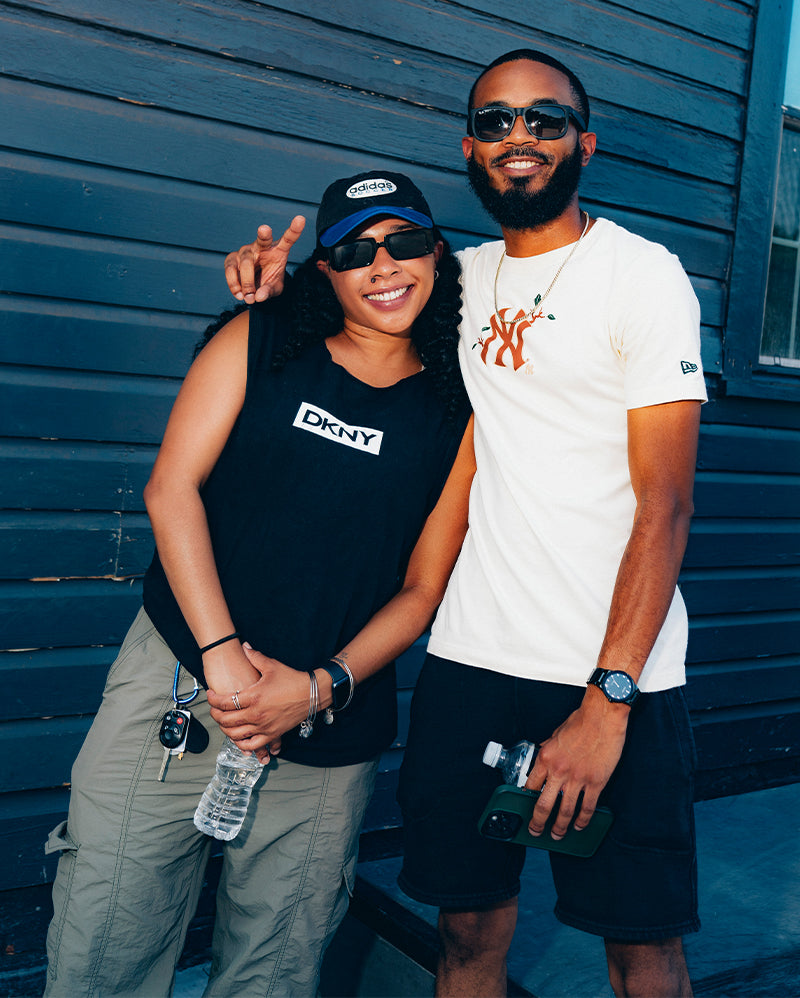 Two people in stylish streetwear posing outdoors, wearing DKNY and New York graphic tops.
