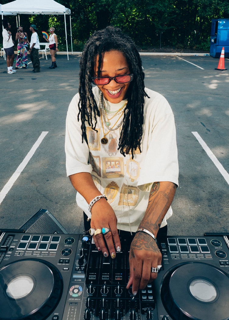 DJ in graphic streetwear mixing music outdoors at a summer event
