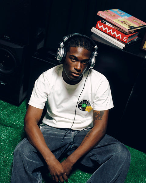 Man in streetwear t-shirt and jeans wearing headphones, sitting on green carpet indoors