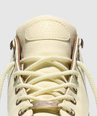 Cream canvas sneaker with metal eyelets and white laces, close-up detail view.