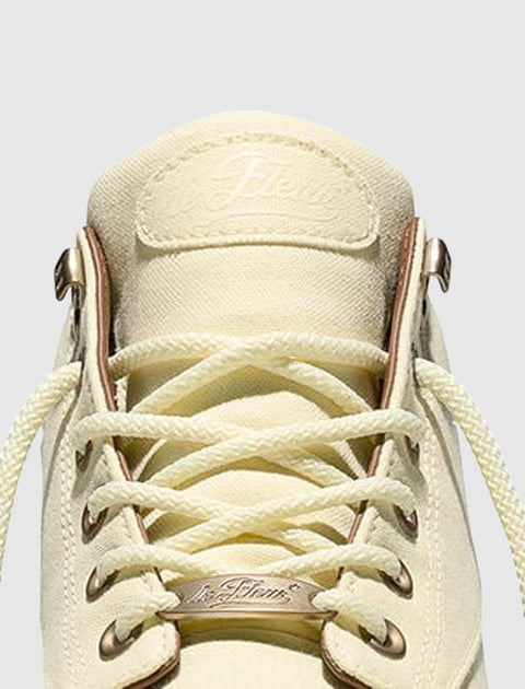 Cream canvas sneaker with metal eyelets and white laces, close-up detail view.