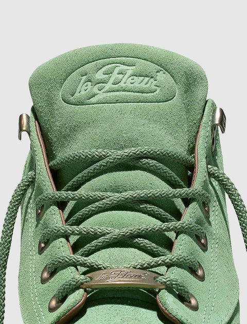 Close-up of green suede sneaker with braided laces and la fleur logo on the tongue