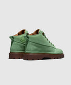 Green suede mid-top boots with brown lugged soles displayed on a light background