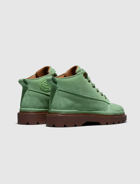 Green suede mid-top boots with brown lugged soles displayed on a light background