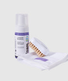Shoe cleaning kit with foam cleaner, brush, and white cloth on a light background
