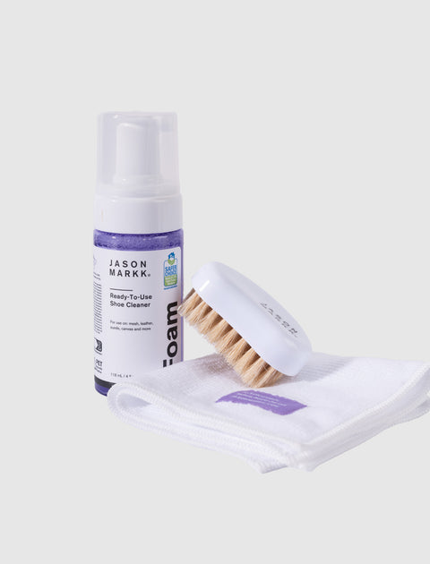 Shoe cleaning kit with foam cleaner, brush, and white cloth on a light background