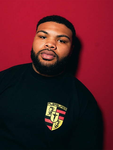 Man modeling black streetwear t-shirt with yellow and red crest graphic on chest