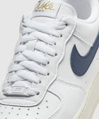 Close-up of white leather low-top sneaker with navy swoosh and gold logo on tongue