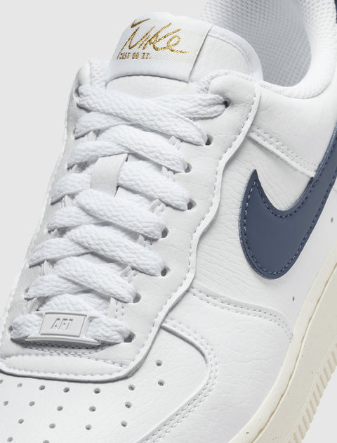 Close-up of white leather low-top sneaker with navy swoosh and gold logo on tongue