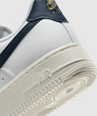 Close-up of white leather low-top sneaker with navy accents and gold branding on heel