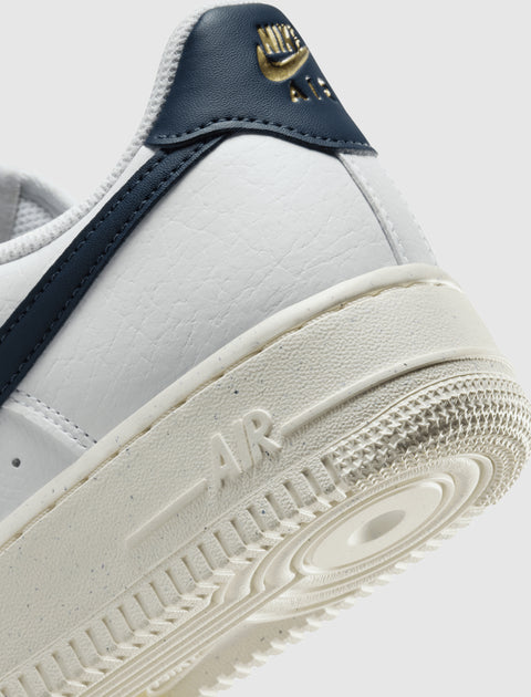 Close-up of white leather low-top sneaker with navy accents and gold branding on heel