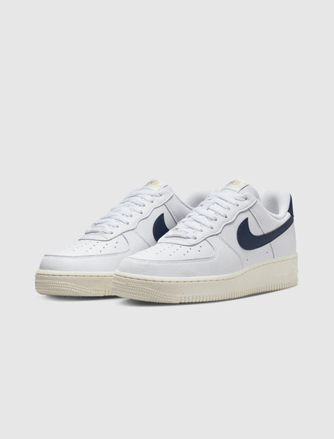 White low-top sneakers with navy swoosh logo and cream sole on light background