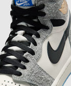 Close-up of a grey and white high top sneaker with black laces and blue Nike Air tongue tag