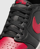 Black and red low-top sneaker with red Nike swoosh and perforated leather toe box