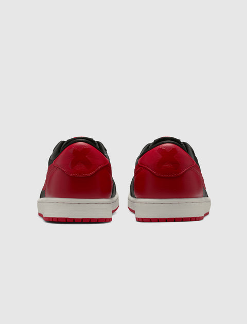 Back view of black and red low-top sneakers with white midsoles on a solid background