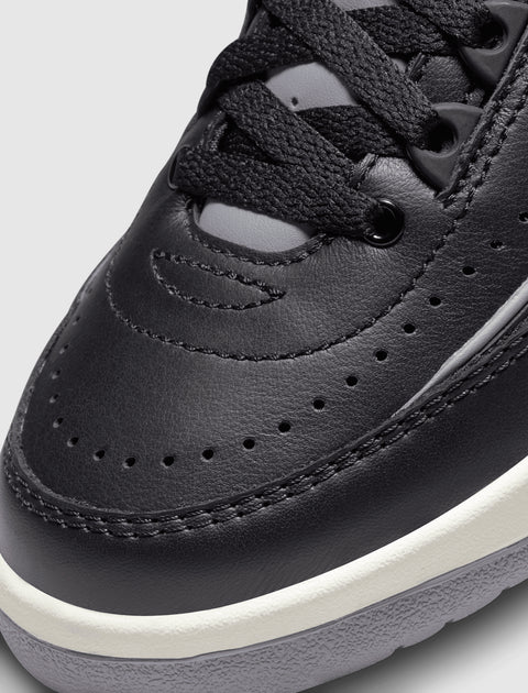 Close-up of black leather sneaker toe with perforated details, black laces, and white sole