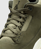 Close-up of olive green sneaker with suede upper, perforated details, and laces.