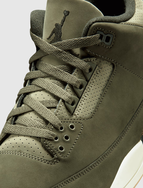 Close-up of olive green sneaker with suede upper, perforated details, and laces.