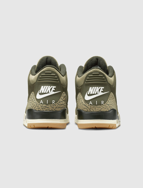 Olive green Nike Air sneakers with gum sole and elephant print heel, rear view.