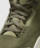 Olive green sneaker close-up with suede upper, textured laces, and Jumpman logo on tongue