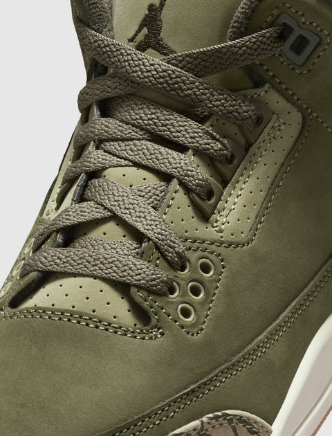 Olive green sneaker close-up with suede upper, textured laces, and Jumpman logo on tongue