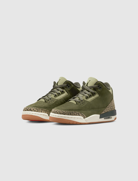 Olive green sneakers with textured beige accents and gum soles on a light background