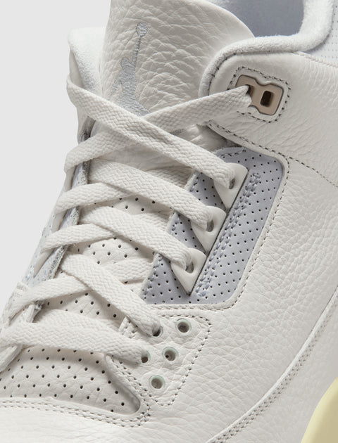 Close-up of white leather sneaker with perforated panels and white laces.