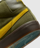 Close-up of olive green suede sneaker with yellow stripe and textured sole