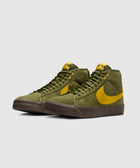 Olive green suede mid-top sneakers with yellow swoosh and brown sole on light background