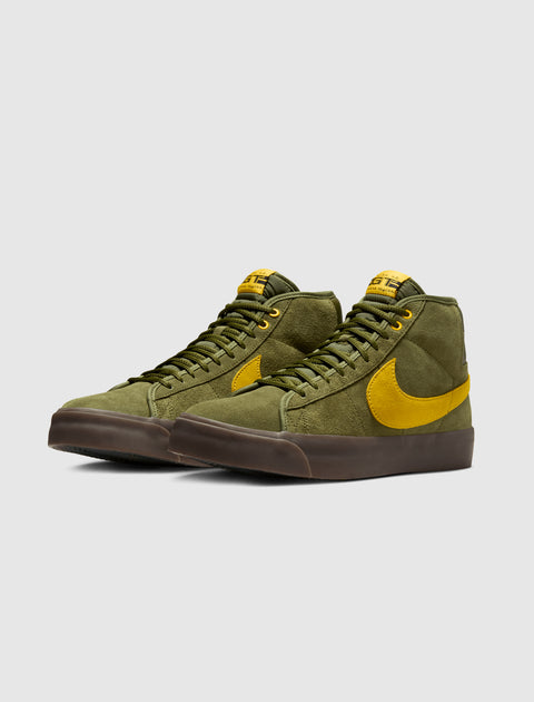 Olive green suede mid-top sneakers with yellow swoosh and brown sole on light background