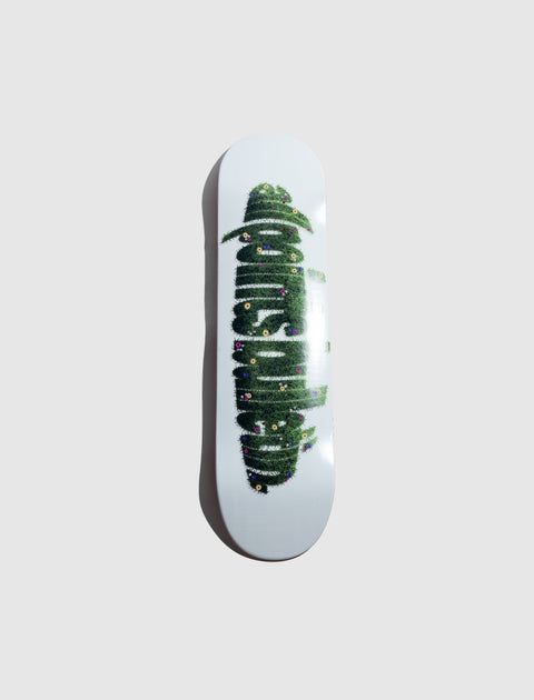 White skateboard deck with green grass and flower graphic design on gray background
