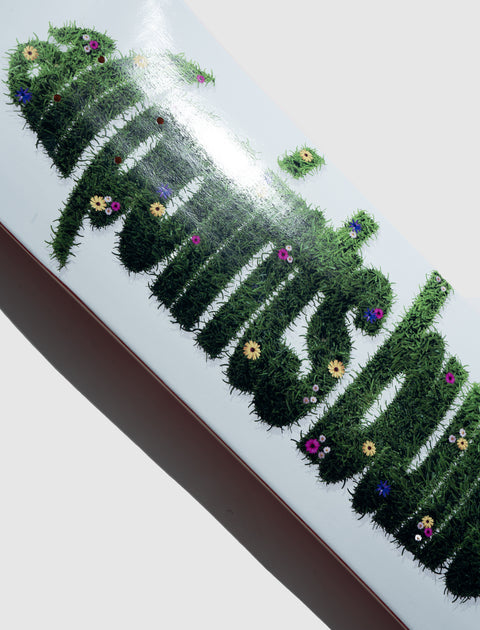 White skateboard deck with green grass and flower graphic lettering design