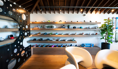 Modern sneaker store interior with wooden shelves displaying athletic shoes, hats, and skateboards.