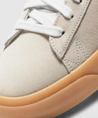 Close-up of beige suede sneaker with white laces and gum rubber outsole