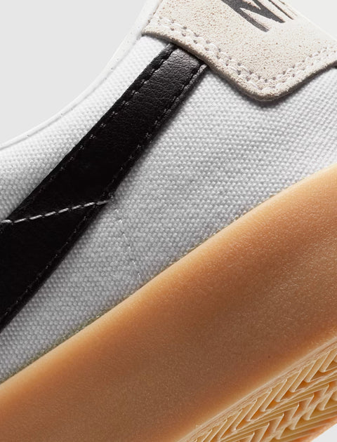 Closeup of white canvas sneaker with black leather detail and gum rubber sole