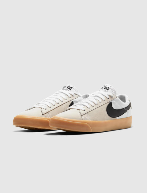 Low-top white and beige sneakers with black swoosh and gum sole on plain background