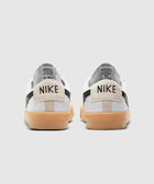 White low-top sneakers with black accents and gum soles, viewed from the back.