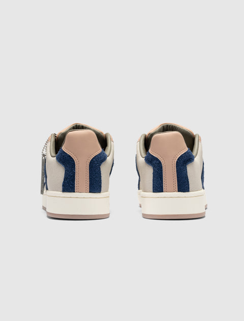 Rear view of beige and navy blue low-top sneakers with tan heel accents on white background
