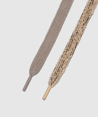 Close-up of two flat shoelaces, one taupe and one beige with black accents, on white background.