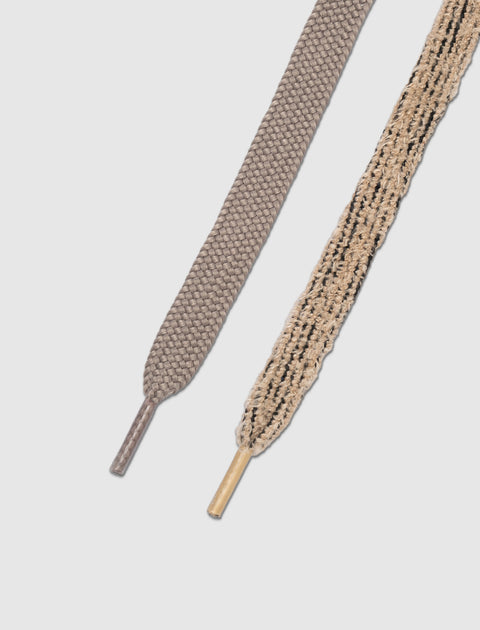 Close-up of two flat shoelaces, one taupe and one beige with black accents, on white background.
