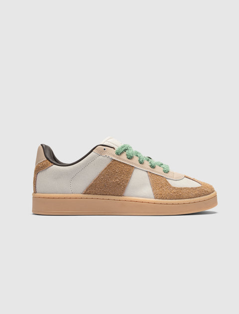 Low top sneaker with cream and brown suede panels, green textured laces, gum sole on white background
