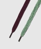 Close-up of two flat sneaker laces, one burgundy and one mint green, on white background