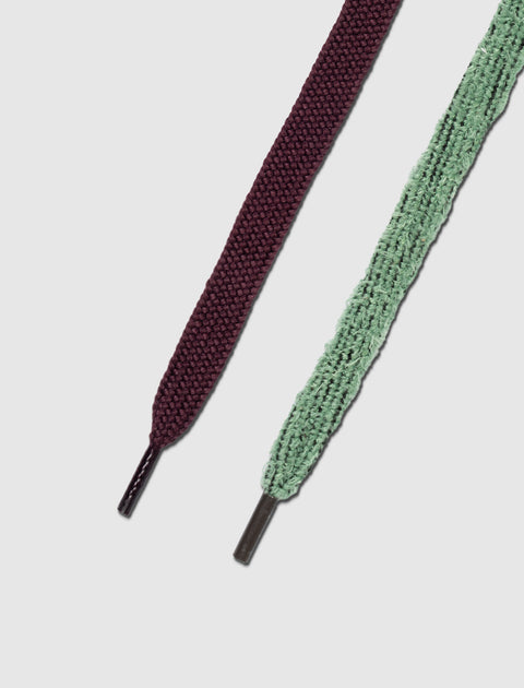 Close-up of two flat sneaker laces, one burgundy and one mint green, on white background