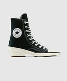Black high-top sneaker with white laces, round logo patch, and unique block heel design.