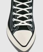 Black canvas sneaker with white laces, white rubber toe cap, and visible stitching