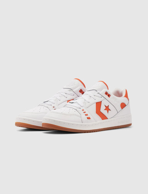 White low top sneakers with orange accents and gum soles on a plain background