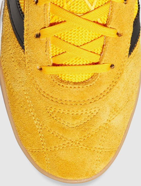 Close-up of yellow suede sneaker toe box with yellow laces and black accents