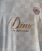 Close-up of Dime Montréal logo on patterned men's streetwear jersey with embroidered crest.