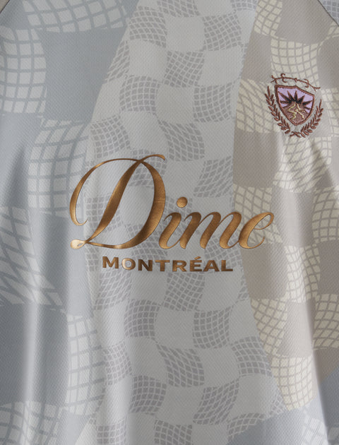 Close-up of Dime Montréal logo on patterned men's streetwear jersey with embroidered crest.